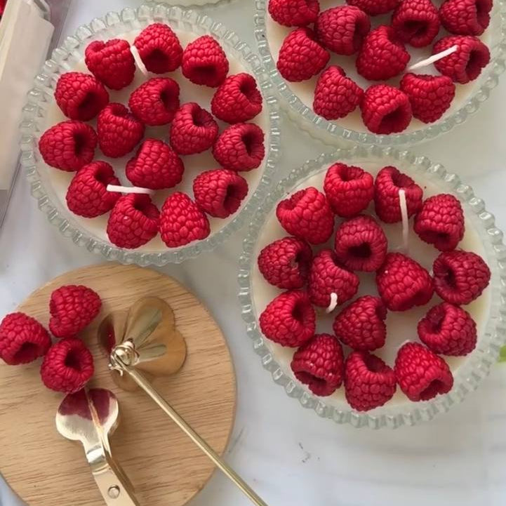 Cupcake candles topped with raspberries on a white plate.